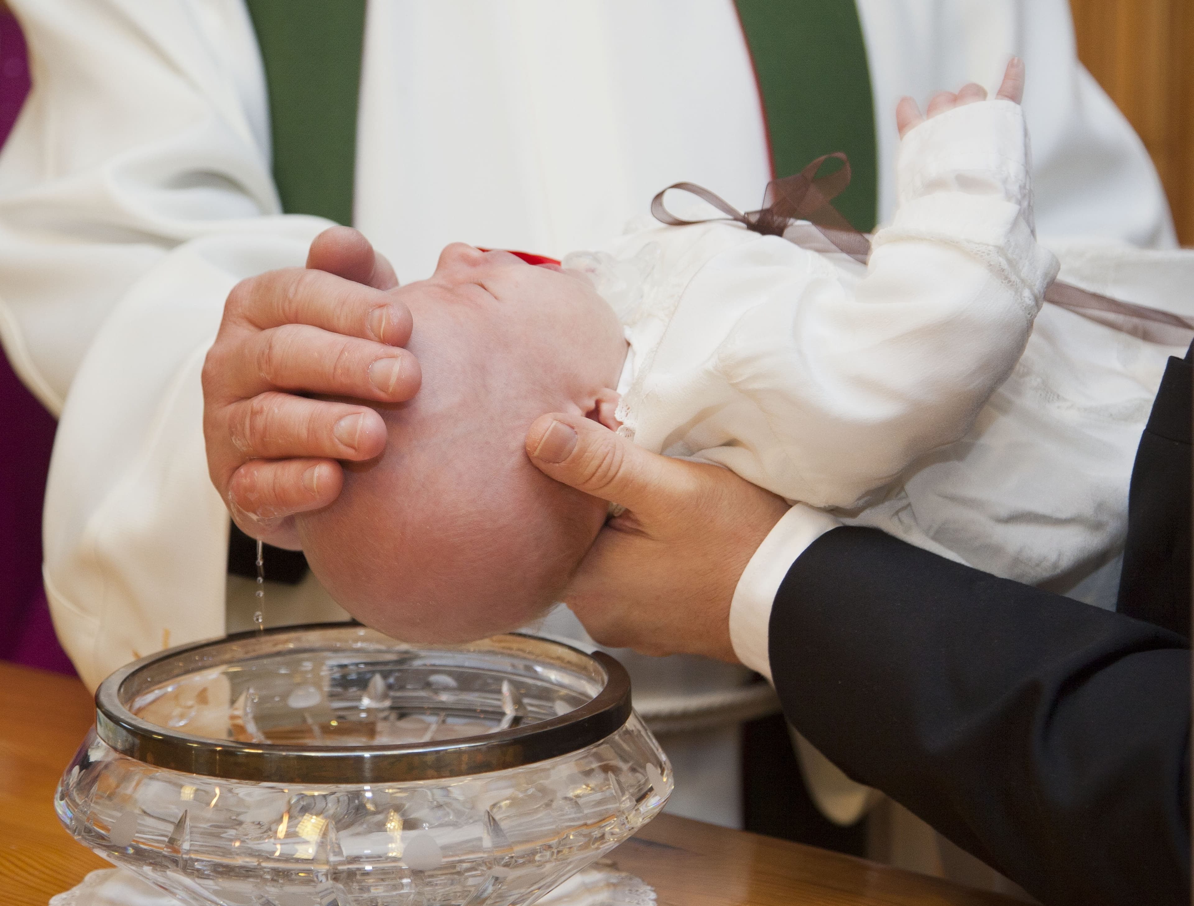 A minister baptises an infant at a church font.